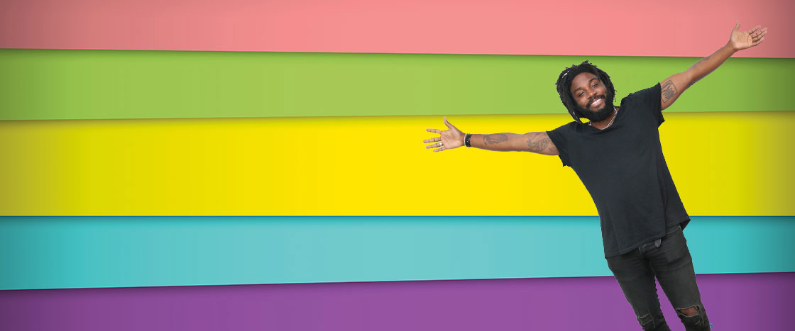 a man smiling with arms wide open in front of a colorful banner