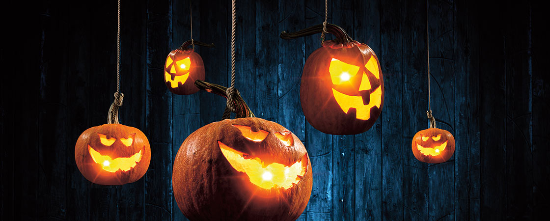Lit pumpkins with carved faces in it hanging by ropes at the stems