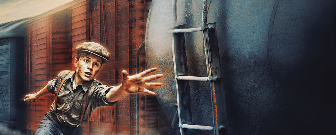 A boy in a cap reaches toward a moving train beside a red boxcar