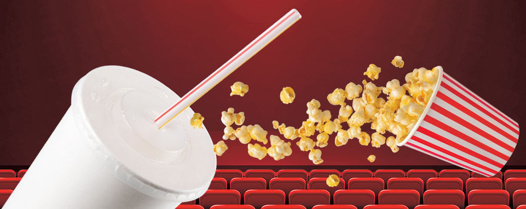 A striped popcorn bucket spills popcorn next to a drink cup in a movie theater