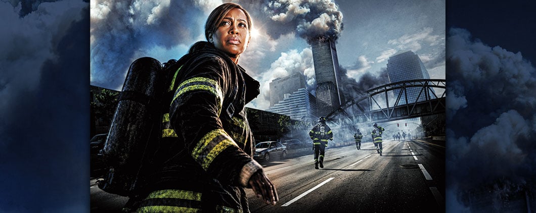 A firefighter stands on a smoke-filled street as others run toward burning city buildings