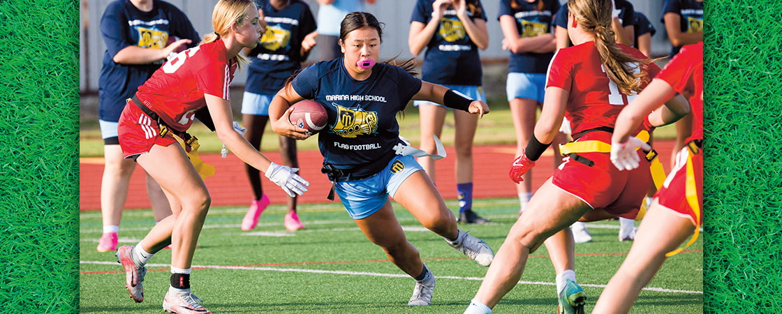 A Marina High School flag football player runs with the ball past defenders on a field